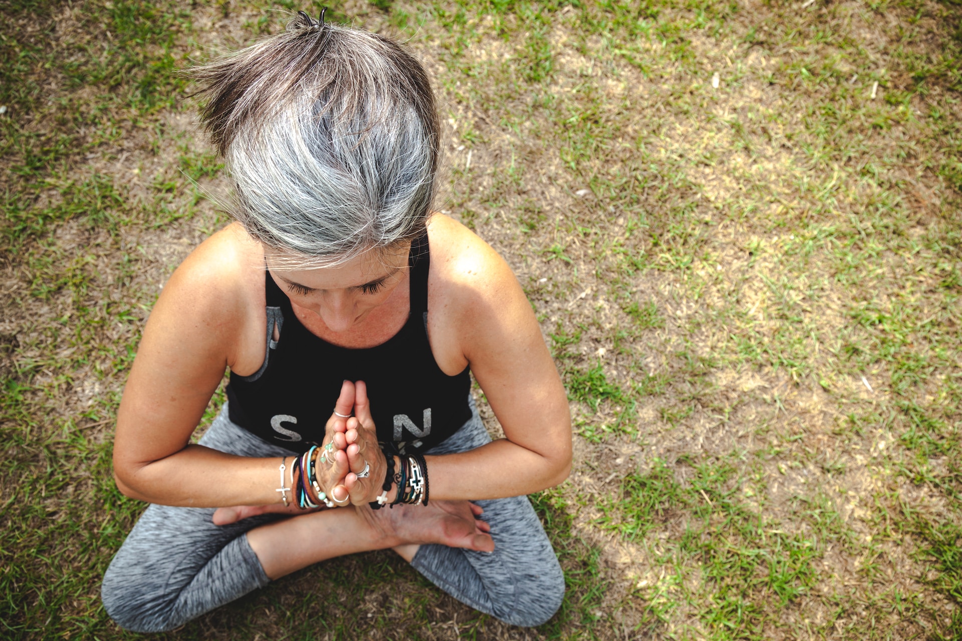 Gray-haired yogi in sitting Sukhasana pose on the grass with prayer Anjali hands