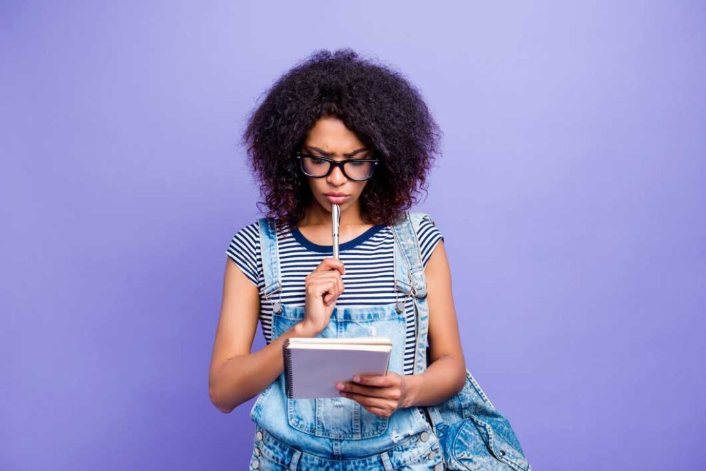Woman looking studiously at a spiral bound notebook in her hand while holding a pen to her bottom lip