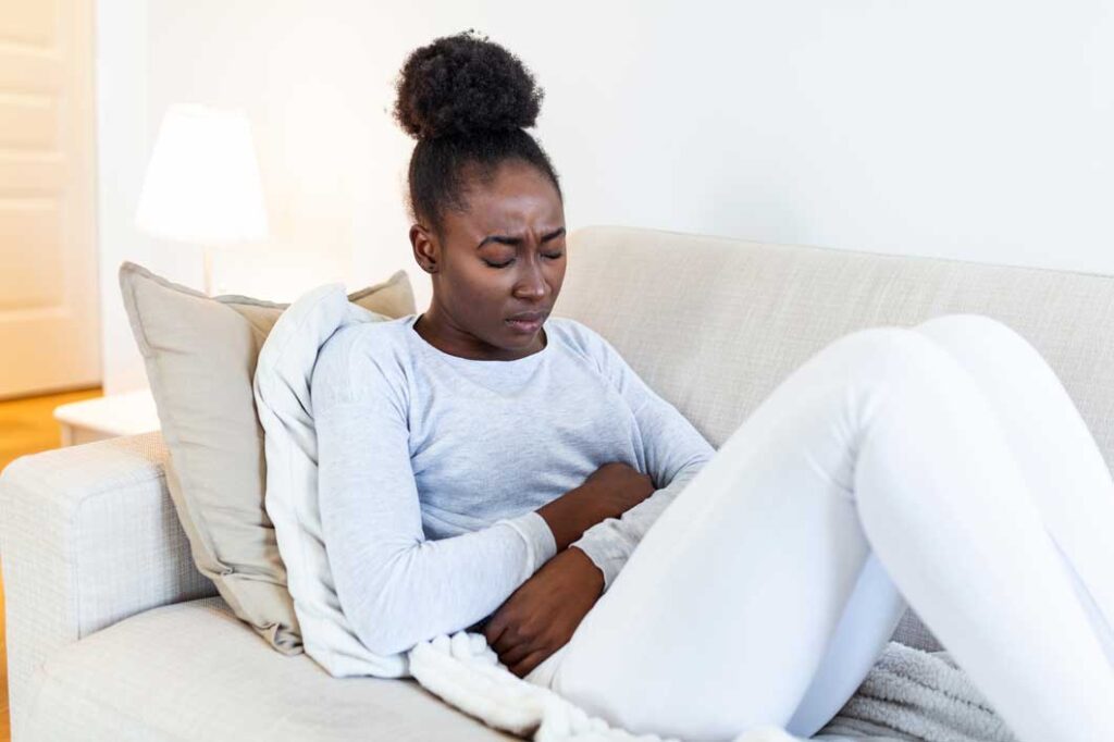 A woman on a couch in pain with her arms across her abdomen and knees pulled in