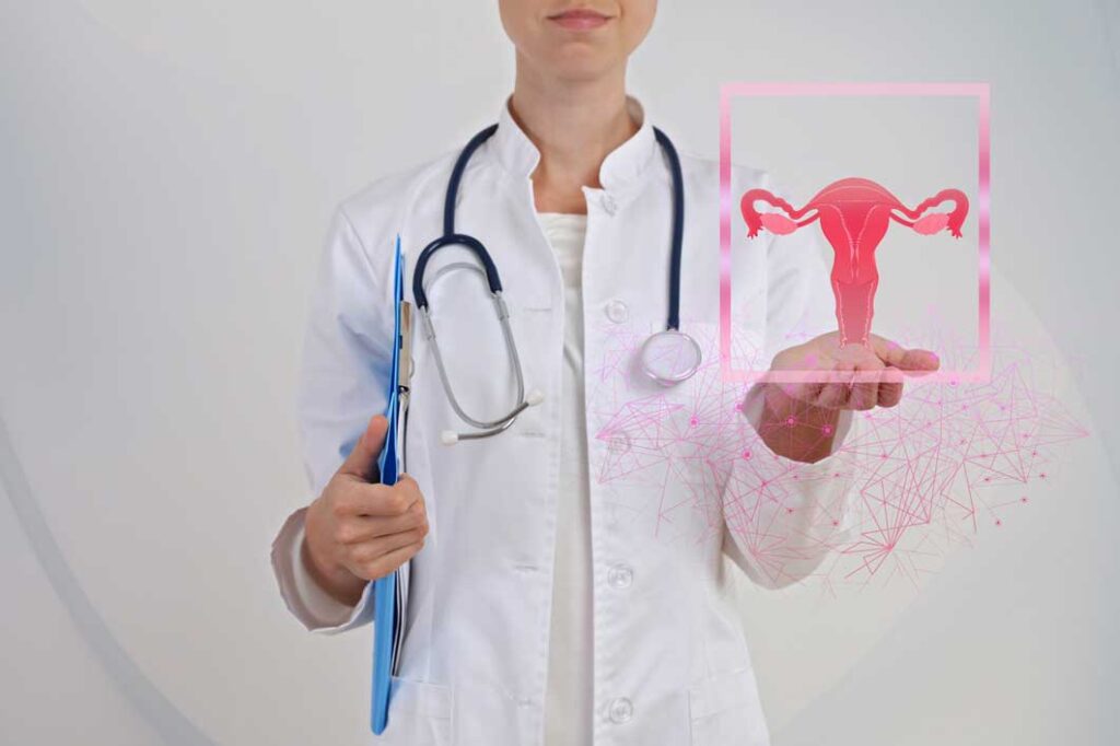 A woman in a doctor's coat with a stethoscope around her neck holding a blue clipboard under one arm and a graphic of a uterus in the other hand